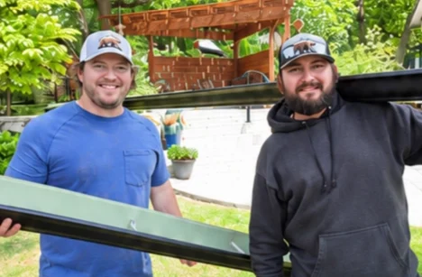 Grizzly Brothers Gutters team members holding seamless gutter sections during a residential gutter installation.
